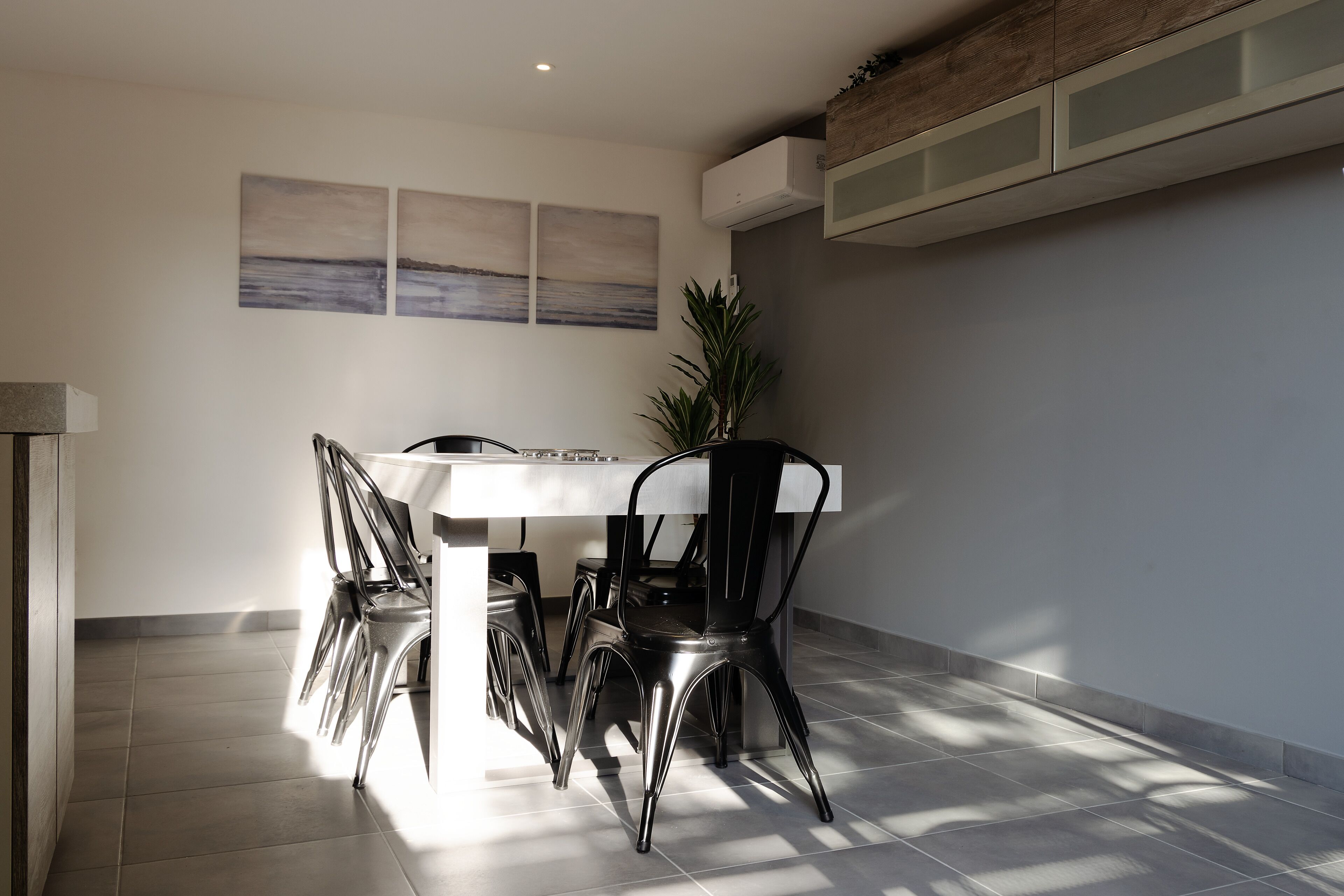 Un espace repas moderne avec une table blanche, des chaises noires et une plante en pot.