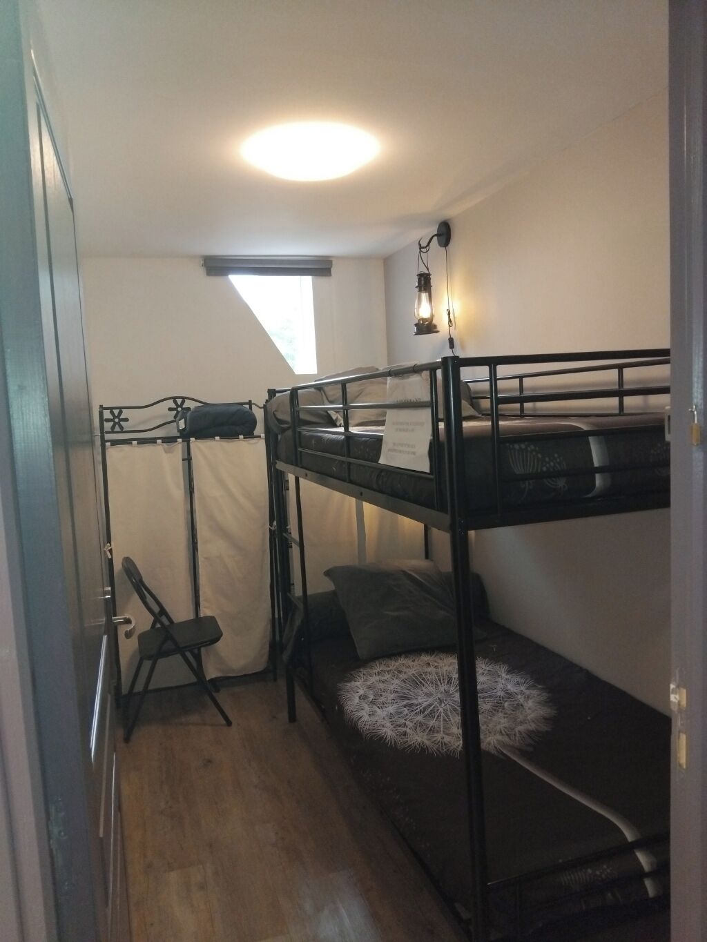 Et værelse med køjeseng, skrivebord, stol, lille vindue og loftslampe.