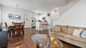 A modern living room with a glass coffee table, a beige sofa, and a dining area with wooden chairs. - 4BR Lucaya Village Home for Big Groups (Osceola County)