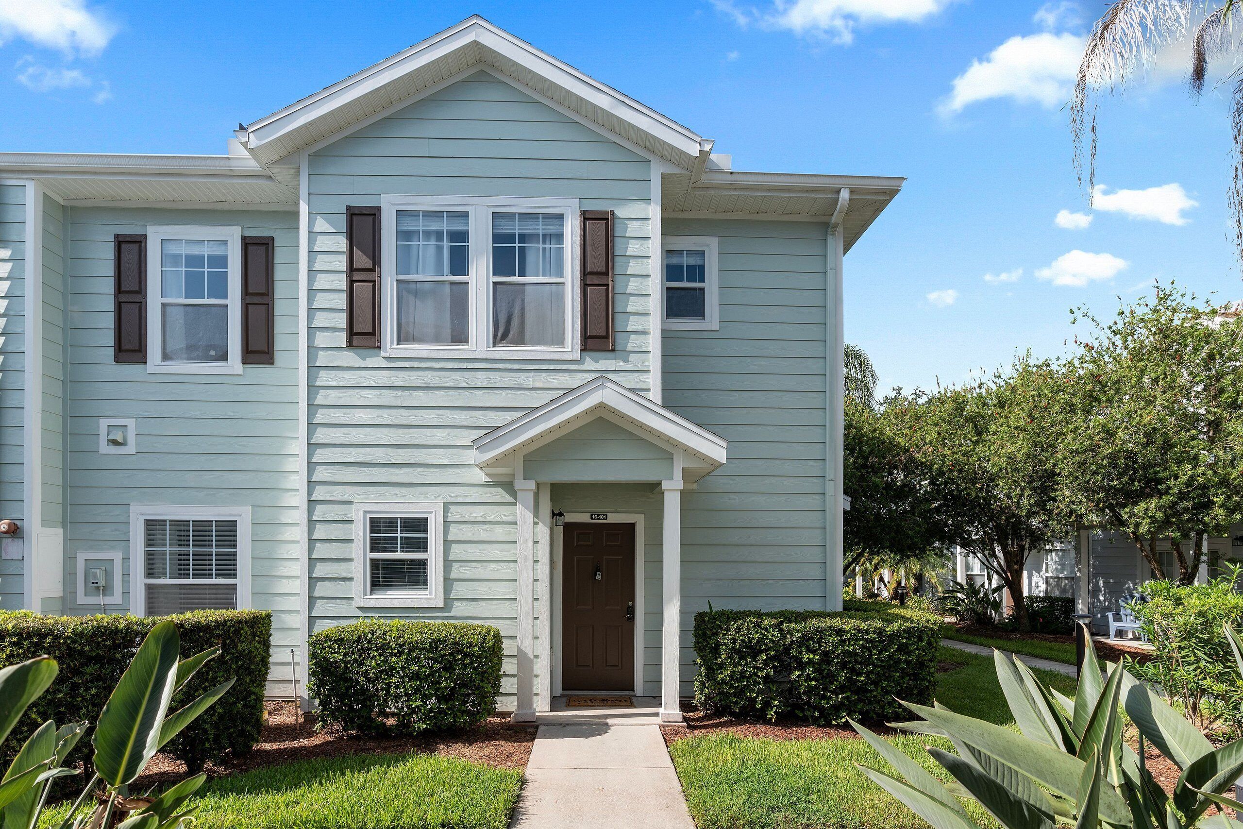 A two-story residential building with a front porch, a central entrance door, and a small front yard with hedges.