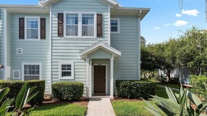 A two-story residential building with a front porch, a central entrance door, and a small front yard with hedges. - 4BR Lucaya Village Home for Big Groups (Osceola County)