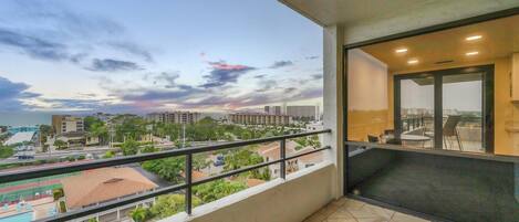 A balcony with a view of a cityscape, a swimming pool, and a building with a glass door.