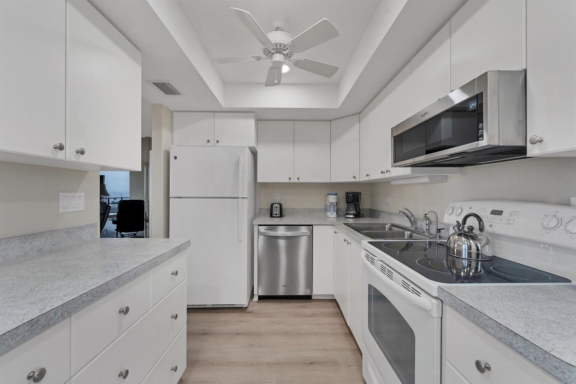 A modern kitchen with white cabinets, a stainless steel refrigerator, a microwave, a kettle, and a dishwasher.