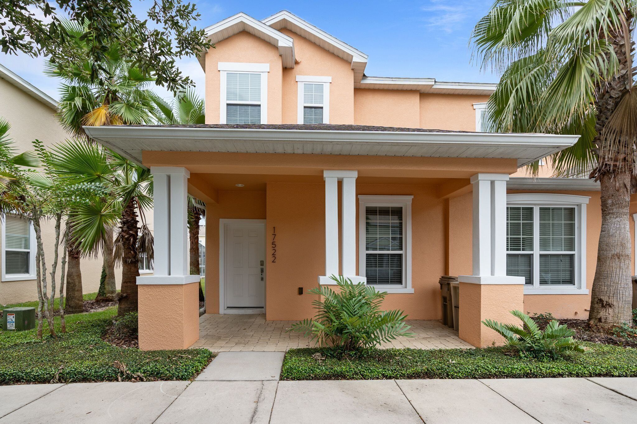 A two-story house with a covered front porch, palm trees, and a well-maintained lawn.