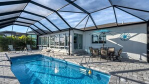 A covered swimming pool with clear blue water, surrounded by a patio area with outdoor furniture and a wall-mounted compass.
