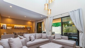 A modern living room with a sectional sofa, ottoman, and a large window with curtains.