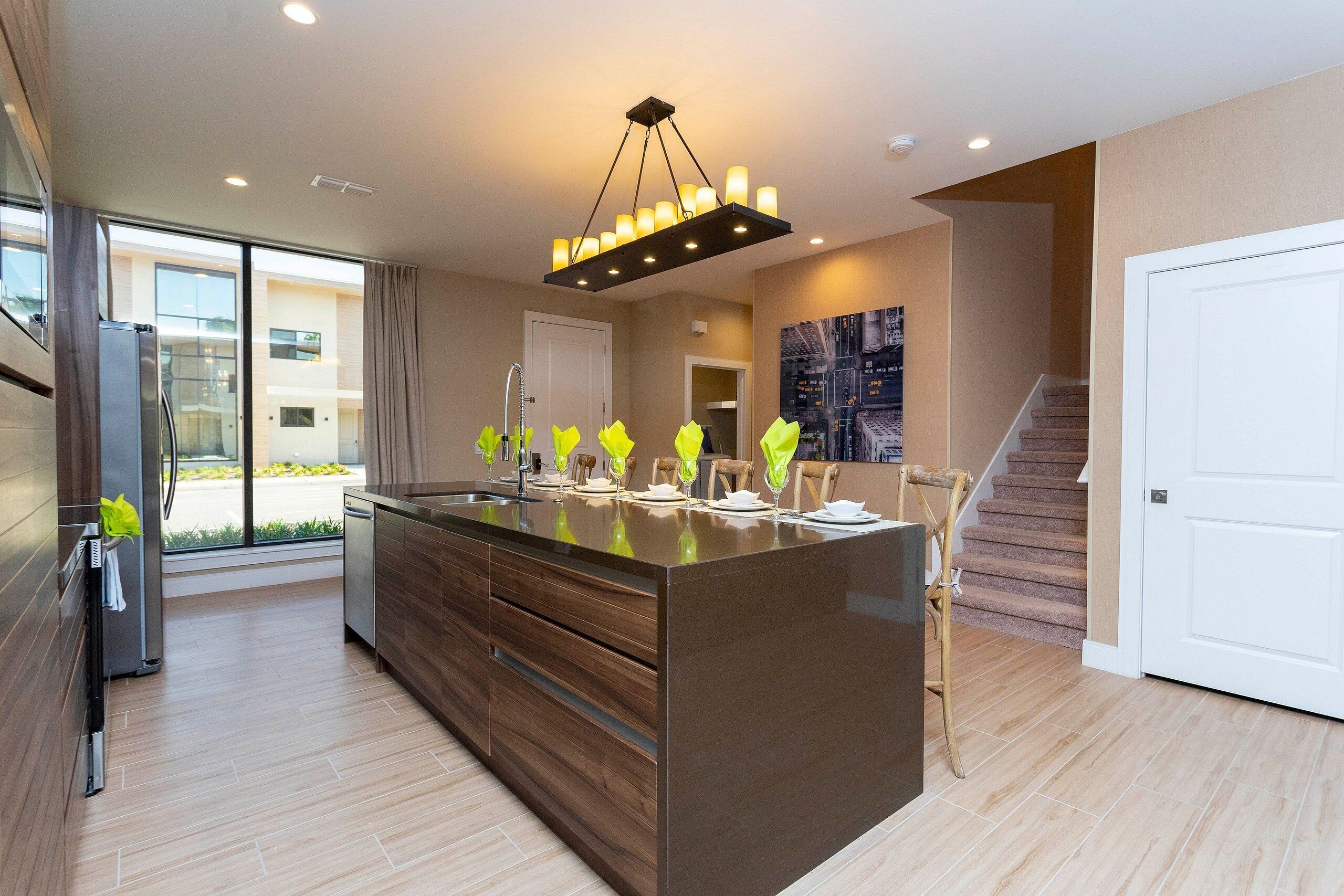 A modern kitchen with a large island, stainless steel appliances, and a contemporary chandelier.