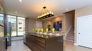 A modern kitchen with a large island, stainless steel appliances, and a contemporary chandelier.