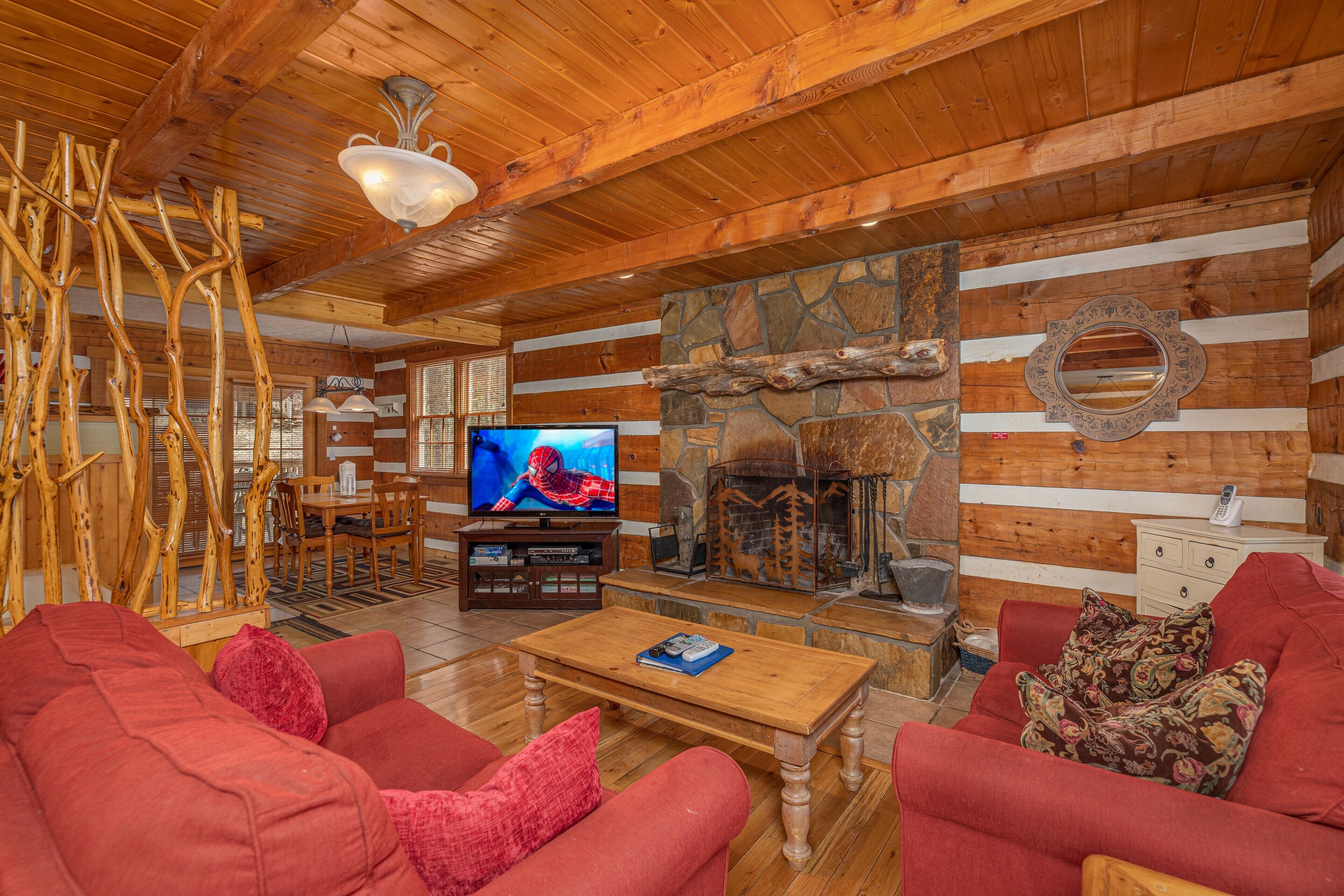 A cozy log cabin interior with a stone fireplace, wooden furniture, and a television in the living area.