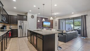 A modern kitchen with dark cabinets, stainless steel appliances, a large island, and a dining area with a view.