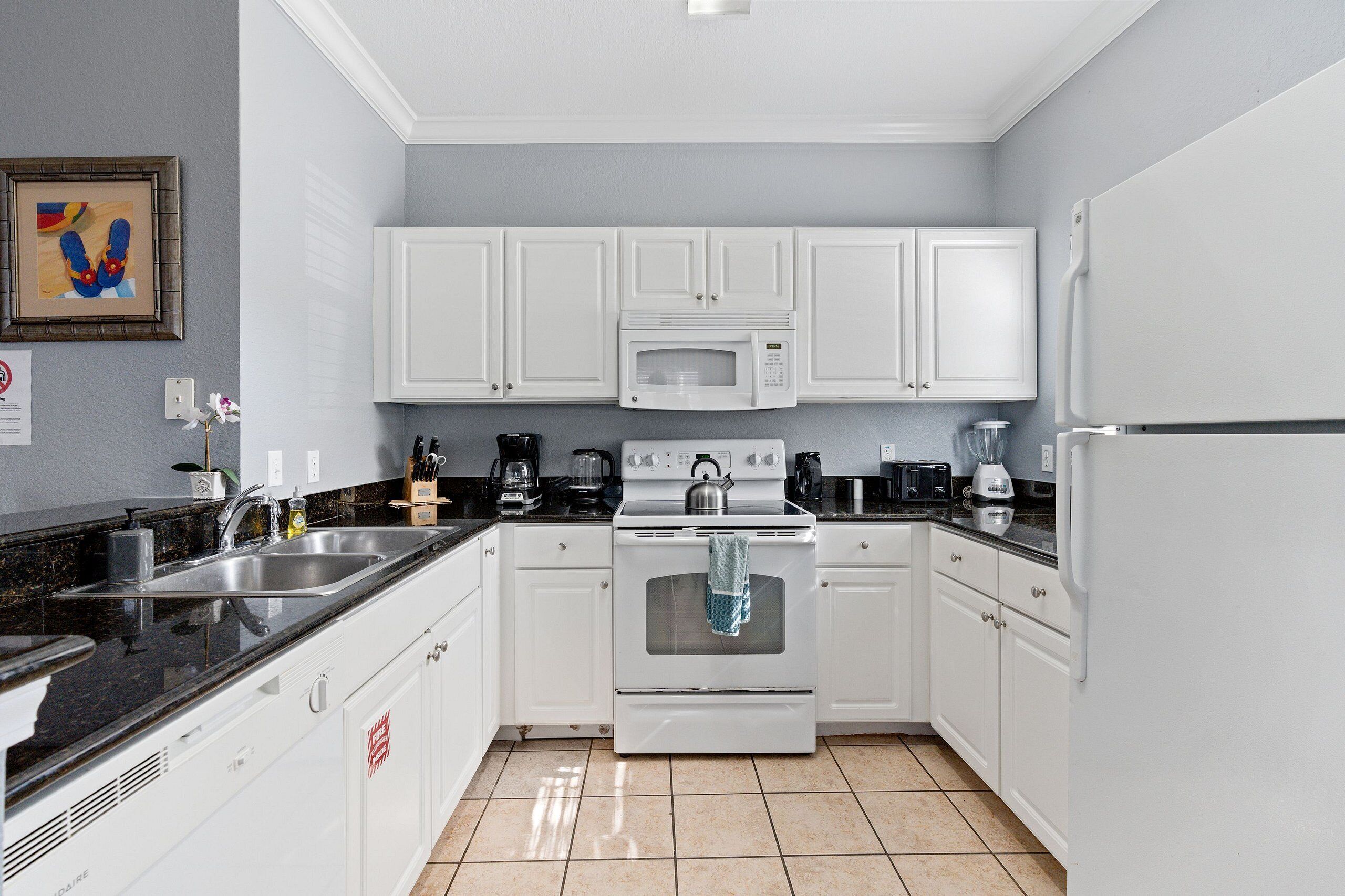 A modern kitchen with white cabinets, a stainless steel sink, a stove, and a microwave.