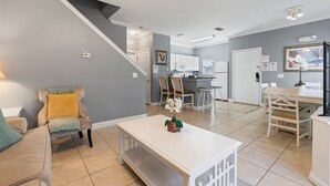 A modern kitchen with white cabinets, a dining area with a white table and chairs, and a staircase leading to another level.