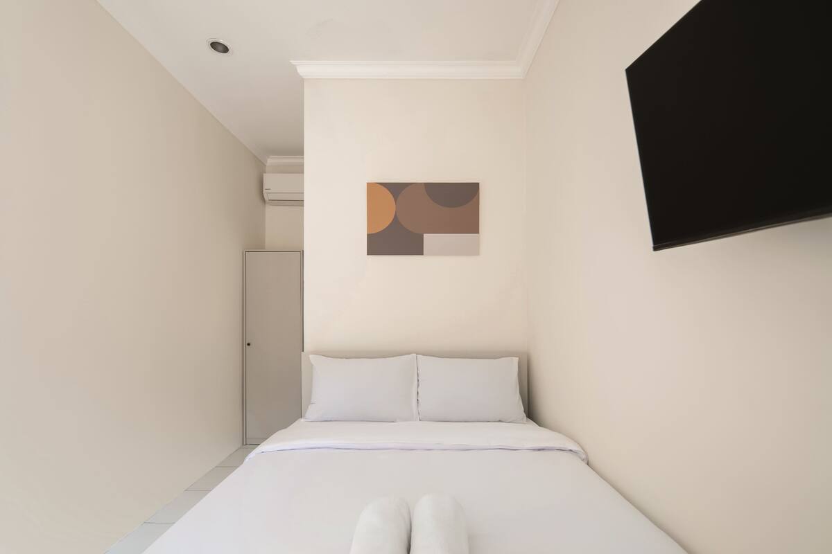 Ein Schlafzimmer mit einem Bett, einem an der Wand befestigten Fernseher und einer Tür zu einem anderen Raum.