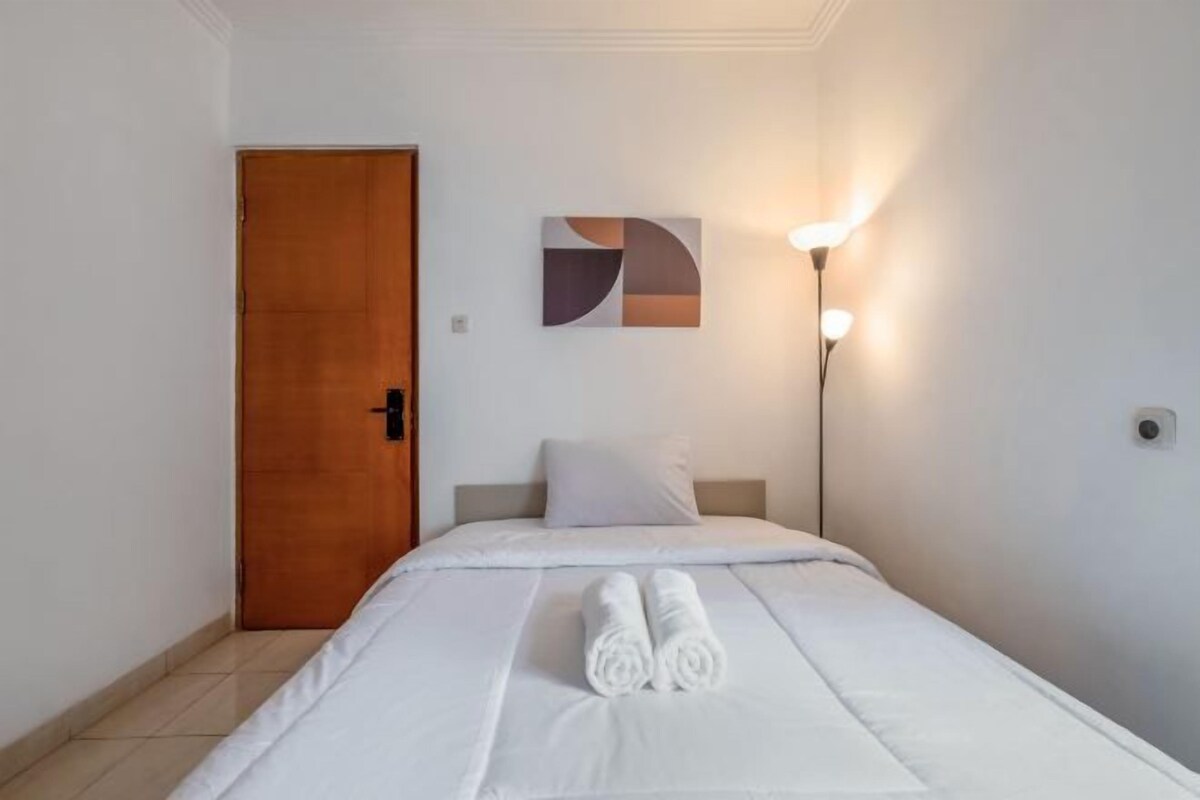 Una habitación de hotel con una cama, una puerta de madera, una obra de arte en la pared y una lámpara de pie.