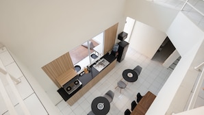 Een moderne keuken met een centraal eiland, zwarte aanrechtbladen en een groot raam. In de eethoek staan twee ronde tafels met stoelen.