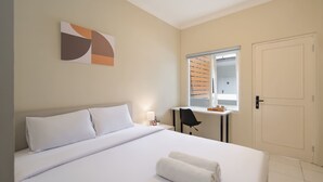 Een hotelkamer met een groot bed, een bureau met stoel, een raam met zonwering en een deur.