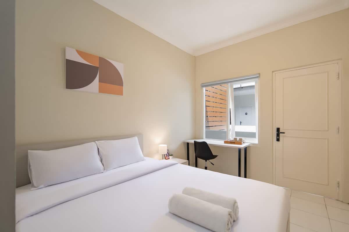 Ein Hotelzimmer mit einem großen Bett, einem Schreibtisch mit Stuhl, einem Fenster mit Jalousien und einer Tür.
