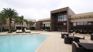 Ein Poolbereich mit Liegestühlen und einem Pool, umgeben von modernen Gebäuden mit großen Fenstern und einer überdachten Terrasse.