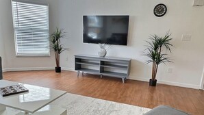 Una sala de estar moderna con un televisor de pantalla plana, una mesa de centro, un sofá gris y dos plantas en macetas.