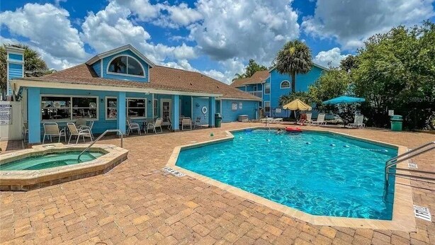 Un área de piscina con una pileta rectangular, sillas de descanso y un edificio de fachada azul.