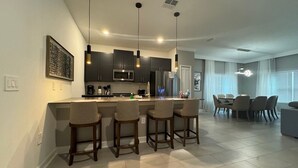 A modern kitchen with a central island, bar stools, and pendant lighting. - 5BR Storey Lake Home, Heated Pool (Kissimmee)