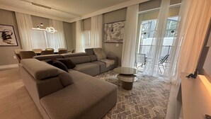 A modern living room with a sectional sofa, a round coffee table, and a dining area with a table and chairs. - 5BR Storey Lake Home, Heated Pool (Kissimmee)