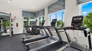 A gym with treadmills, weight machines, and a large window with a view of palm trees. - 5BR Storey Lake Home, Heated Pool (Kissimmee)
