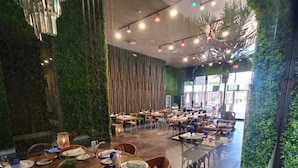 Een restaurant met meerdere eettafels gedekt voor gasten, met een modern interieur en groene wanden en een kroonluchter.