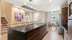 Een moderne keuken met een groot eiland, houten kasten en een zithoek met stoelen.