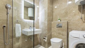 A modern bathroom with a glass-enclosed shower, a sink, a toilet, and a washing machine. - Princess Milena Apartments - Apartment Milena (Bečići)