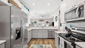 A modern kitchen with stainless steel appliances, white cabinetry, and a wooden floor. - Palm Beach Oasis (Panama City Beach)