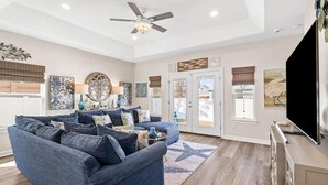 A spacious living room with a large blue sectional sofa, a ceiling fan, and a flat-screen TV. - Palm Beach Oasis (Panama City Beach)