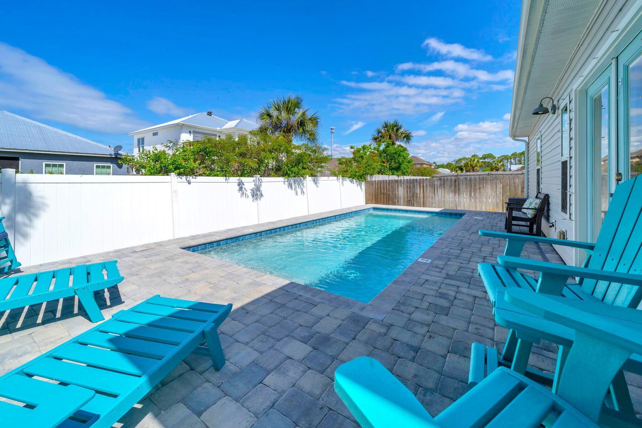 A backyard with a swimming pool, blue lounge chairs, and a wooden fence.