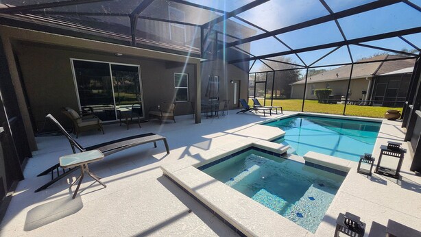Un espace piscine doté d’une structure en verre, de chaises longues et d’un jacuzzi.