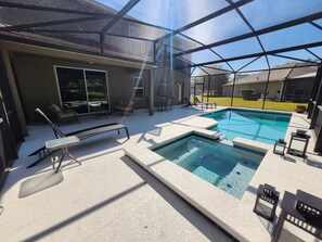 A pool area with a glass enclosure, lounge chairs, and a hot tub. - Amazing 5BD/5BA House with Pool and TV Near Disney (Kissimmee)