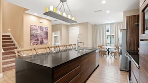 A modern kitchen with a large island, wooden cabinetry, and a dining area with chairs. - Magic Village Charming special 6 min Disney (Kissimmee)