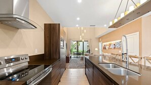 A modern kitchen with a stainless steel range hood, double sink, and a wooden accent wall. - Magic Village Charming special 6 min Disney (Kissimmee)