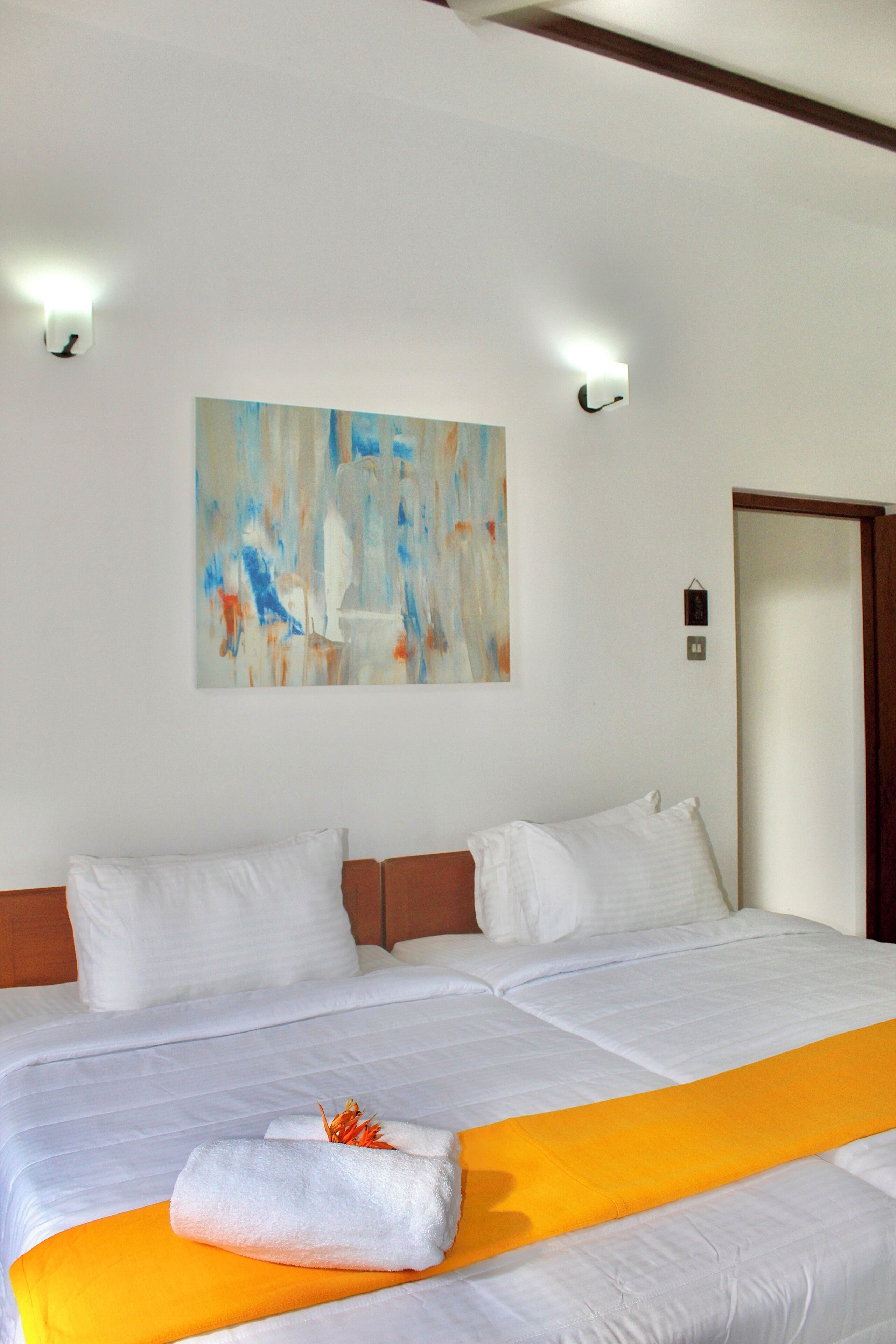 Ein Hotelzimmer mit einem großen Bett, weißer Bettwäsche, einem gelben Zierkissen und einem Gemälde an der Wand.