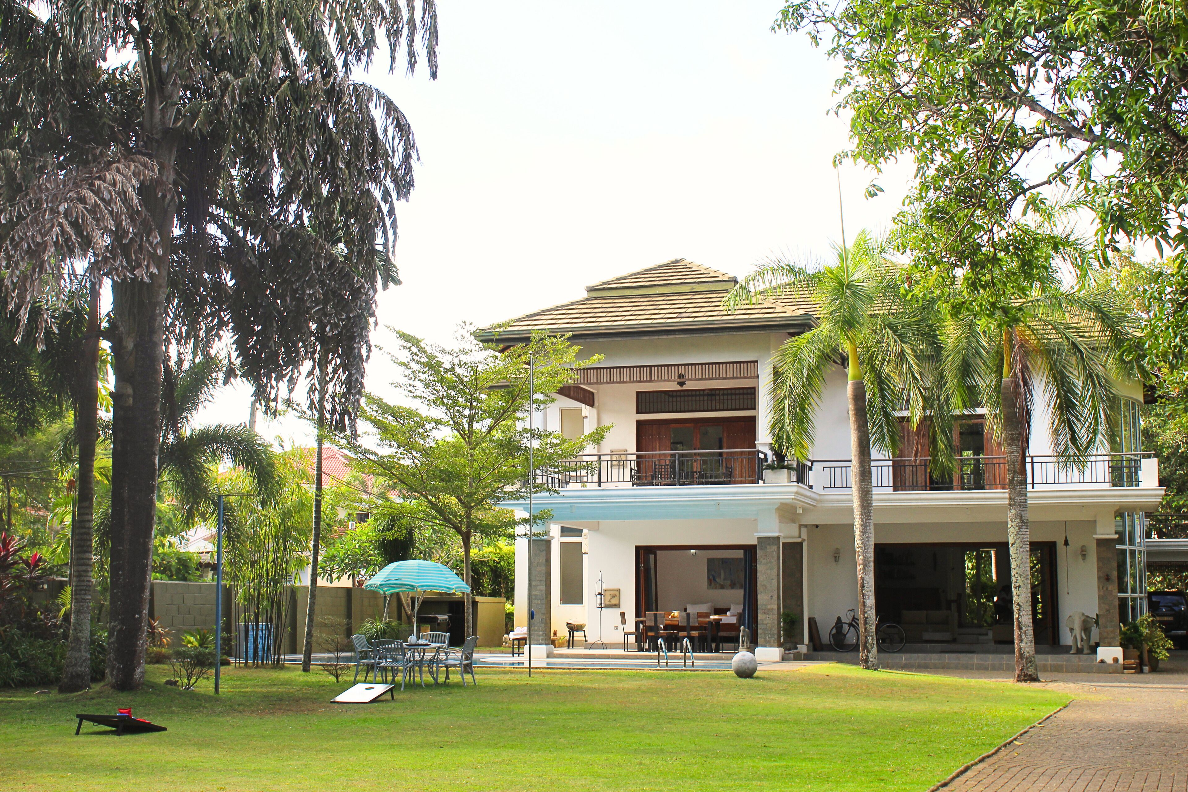 A two-story building with a balcony, surrounded by palm trees and a grassy lawn.