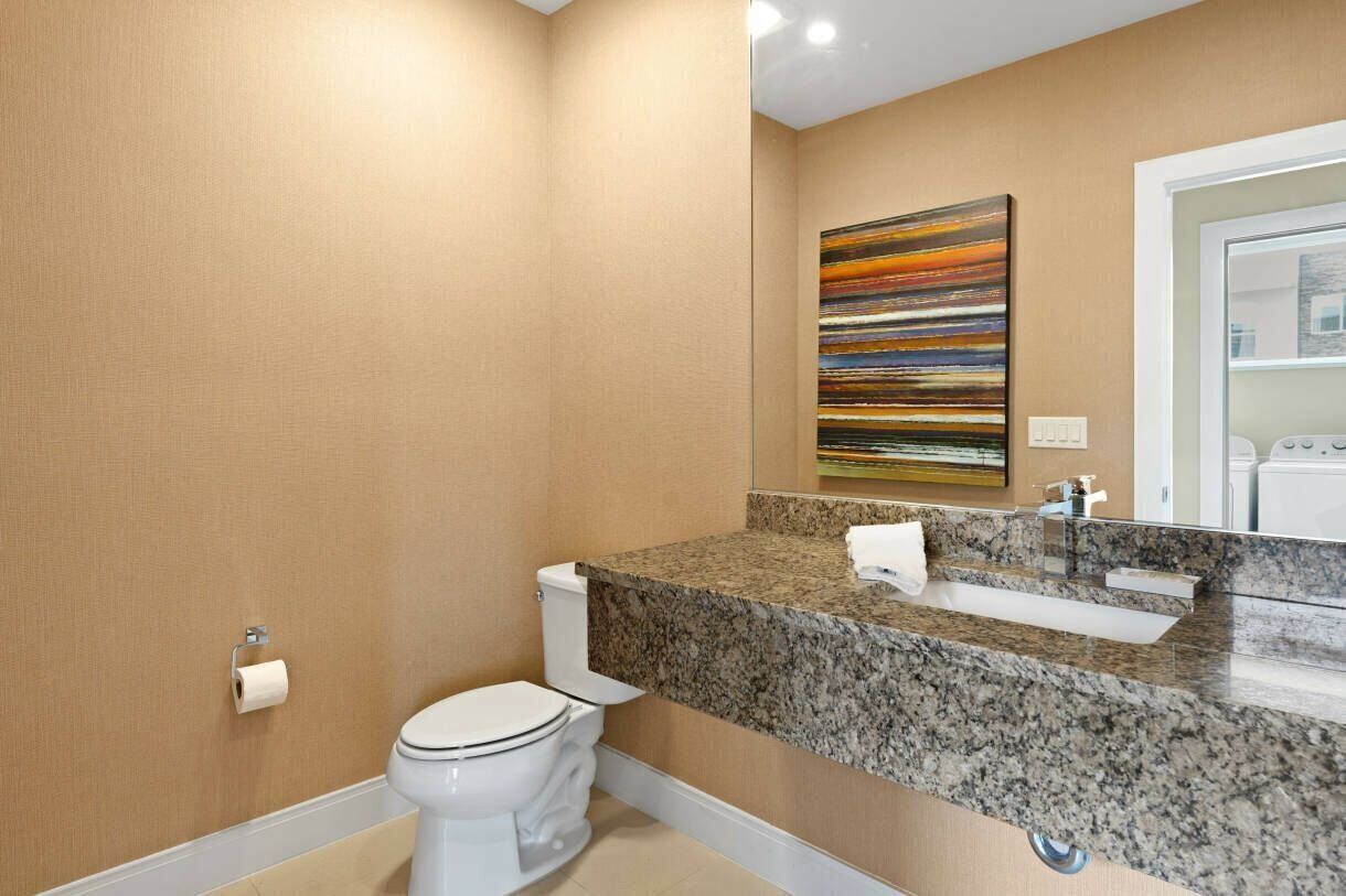 A modern bathroom with a toilet, granite countertop, sink, and a large mirror.