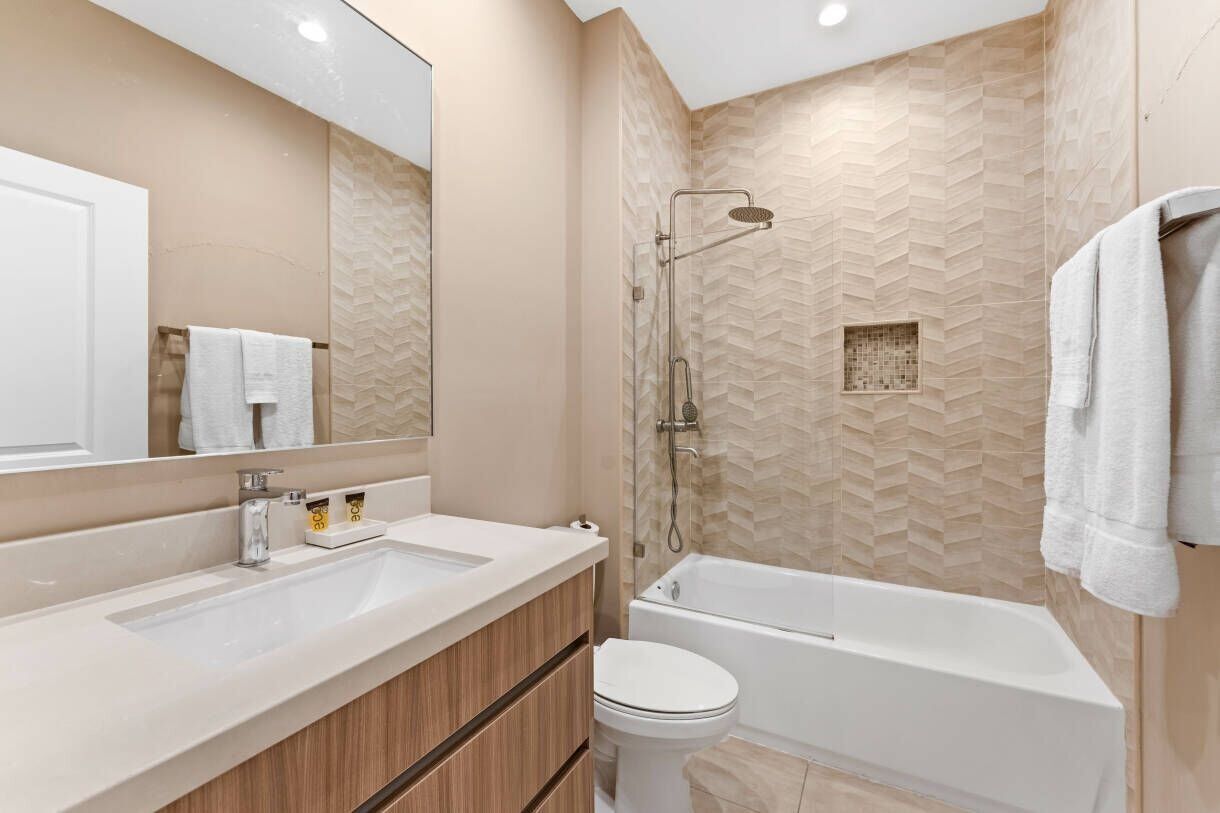 Une salle de bain moderne avec un grand miroir, deux lavabos, des toilettes et une baignoire.