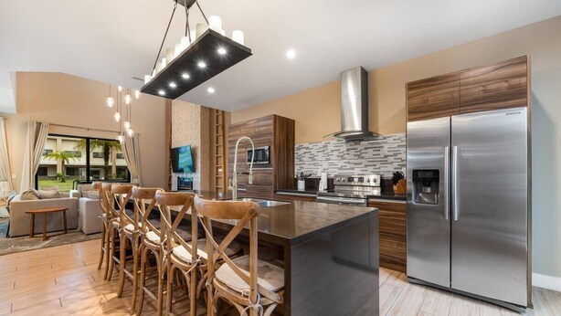 A modern kitchen with a large island, stainless steel appliances, and a dining area with wooden chairs.