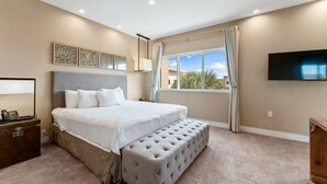 A bedroom with a large bed, a bench, a TV, and a window with curtains.