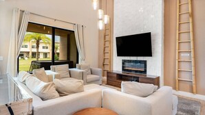 A modern living room with a flat-screen TV mounted on a white brick wall, a wooden TV stand, and a large sectional sofa with multiple cushions.