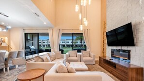 A modern living room with a large flat-screen TV, beige sofas, and a wooden entertainment unit.