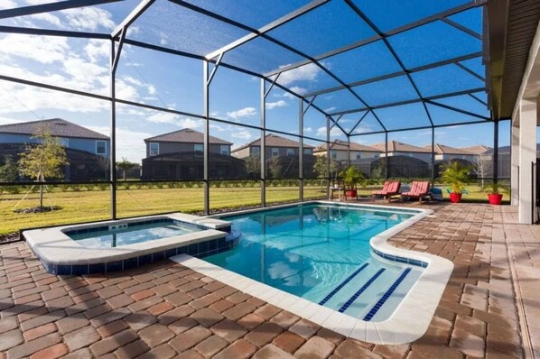 A backyard with a swimming pool, hot tub, and patio area with chairs and potted plants.