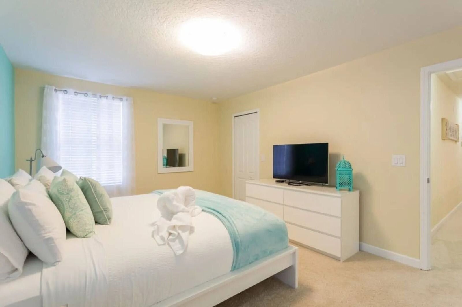 A bedroom with a bed, a TV on a dresser, a mirror, and a door.