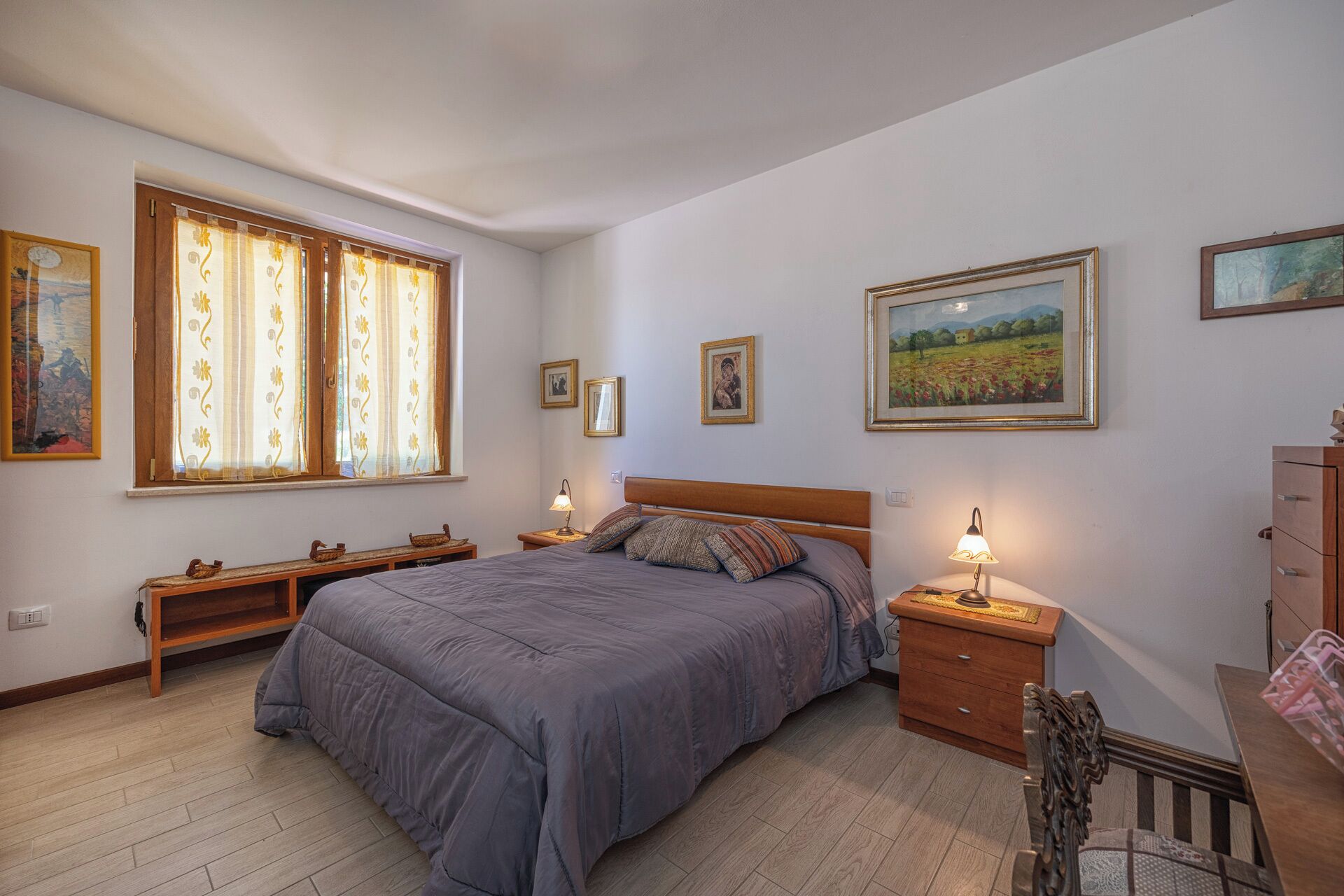 Quarto com uma cama grande, duas mesas de cabeceira, um banco de madeira e um aparador.