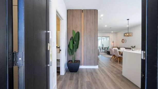 A modern interior with a hallway leading to a dining area, featuring a large potted plant and wooden paneling.