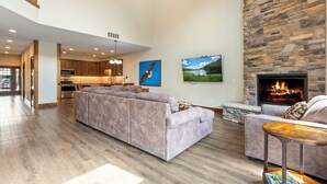 A spacious living room with a stone fireplace, a large sectional sofa, and a television mounted on the wall.